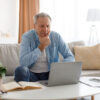 Wenn die Rente nicht reicht Boomer – nachdenklicher Mann 60+ mit Laptop am Schreibtisch, warmes Licht