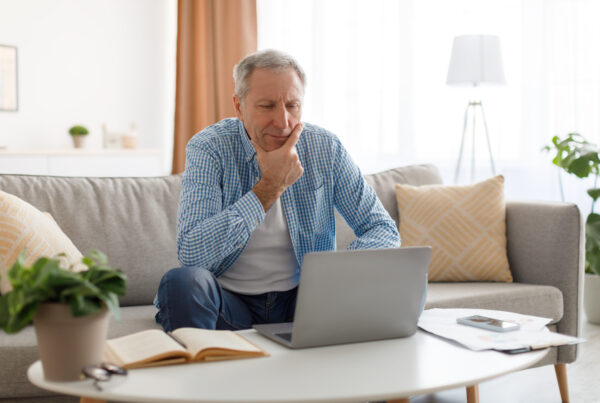 Wenn die Rente nicht reicht Boomer – nachdenklicher Mann 60+ mit Laptop am Schreibtisch, warmes Licht