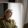 Self-Directed Ageism Boomer – nachdenkliche Frau 60+ vor einem Spiegel, der eine jüngere Version zeigt